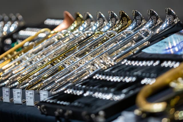 Rows of polished trumpets and trombones displayed in black cases on a trade stand