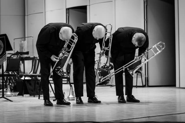 Three trombonists bowing on stage holding their instruments in a black-and-white photo