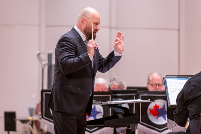 A conductor with baton raised leads a brass band on stage