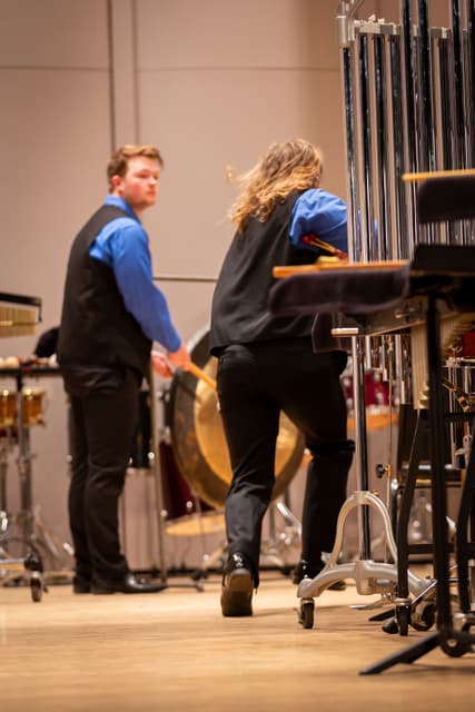 Two percussionists on stage near tubular bells and a gong, holding mallets