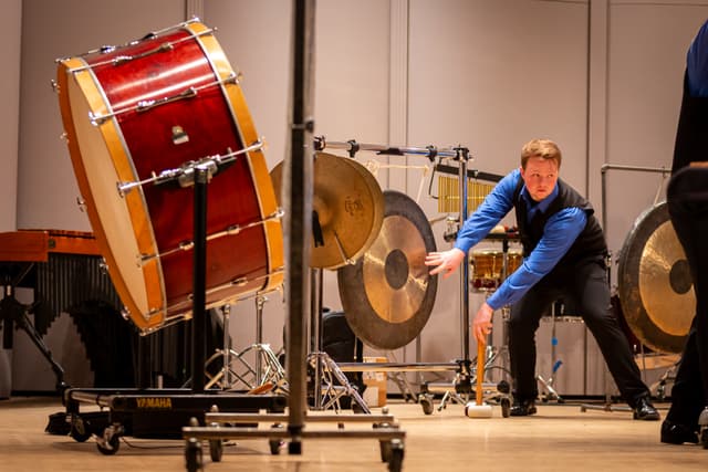 Percussionist reaching toward a gong beside a large red bass drum on stage