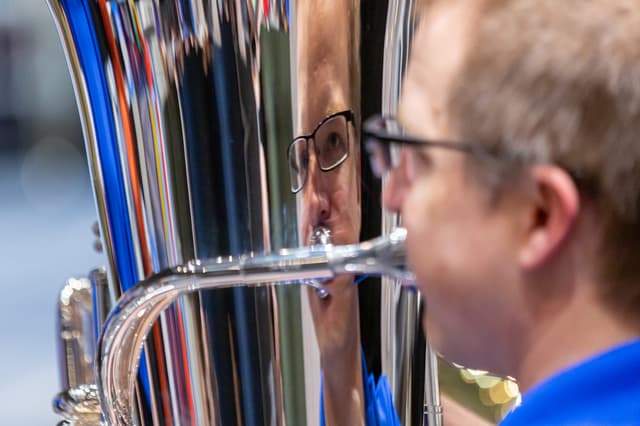 Close-up of a tuba player with his face reflected in the instrument's silver bell