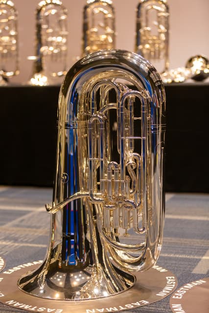Silver tuba standing on an Eastman-branded disc with other instruments blurred behind it
