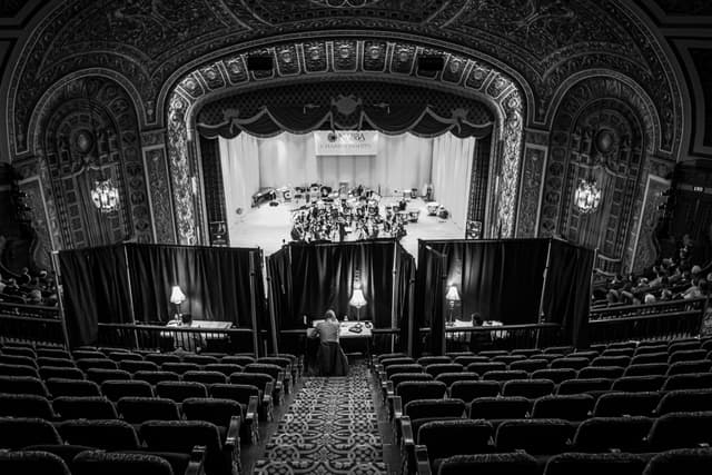 Black and white view from theatre balcony of adjudicators' booths and a brass band on stage