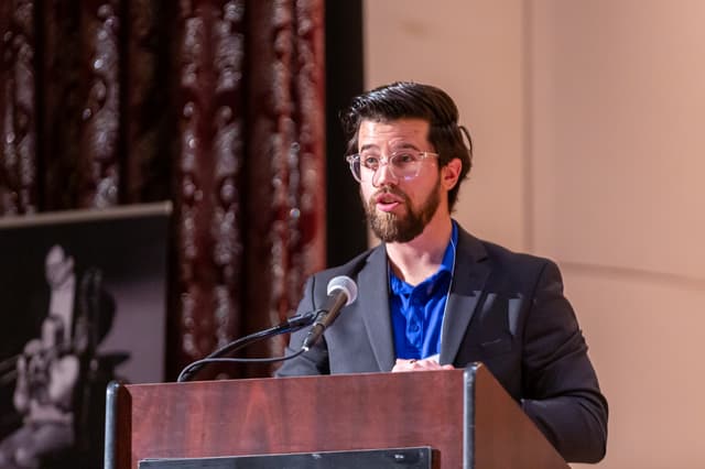 Speaker at a wooden lectern with microphone in front of a curtain