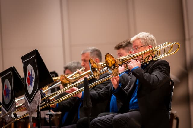 Row of trombonists performing on stage with slides extended beside NABBA-branded music stands