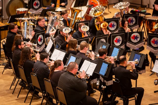 Brass band performing on stage, cornet players in front, tubas and percussion behind