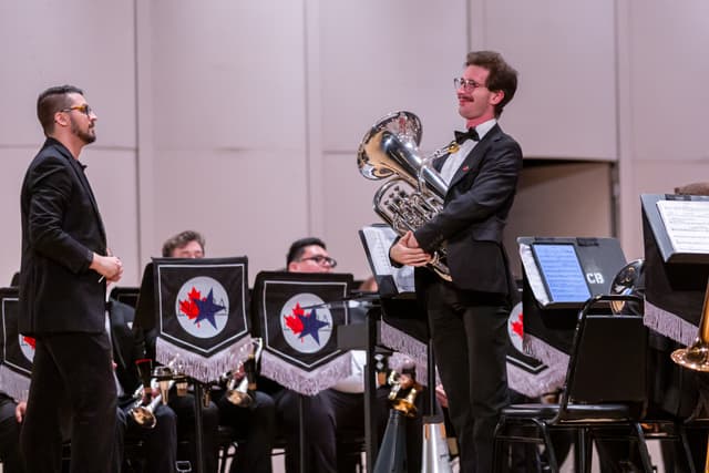 Euphonium player smiling at a conductor on stage in front of a seated brass band
