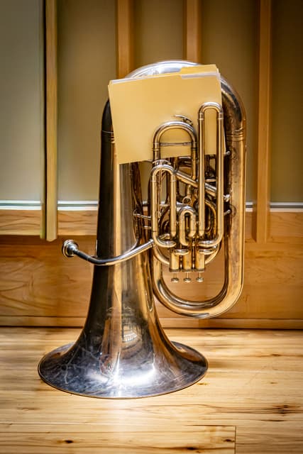 Silver Yamaha tuba on a wooden floor with a music folder resting on it