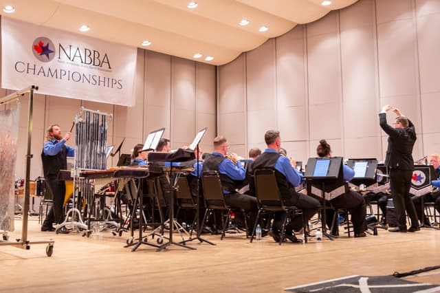 Brass band performing on stage under a NABBA Championships banner with conductor and percussionist