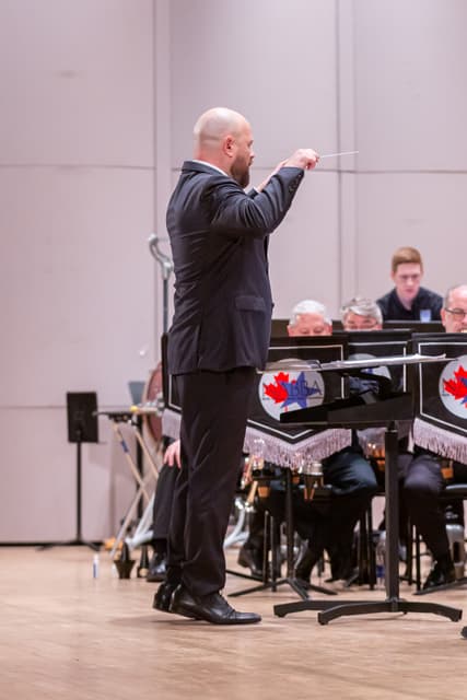 Conductor with raised baton leads a seated brass band on stage