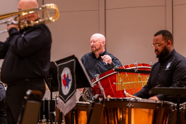 Trombonist and percussionists performing on stage with timpani, bass drum and chimes