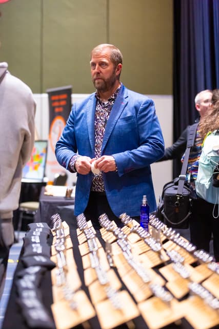Man in blue blazer behind a table of mouthpieces on wooden display boards