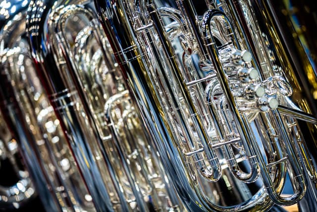 Close-up of polished silver tubas with valves and curved tubing, background instruments softly blurred