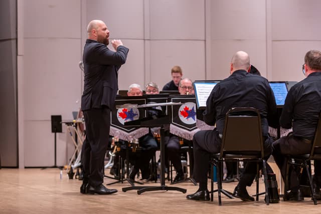 Conductor leading a seated brass band on stage with NABBA banners on music stands