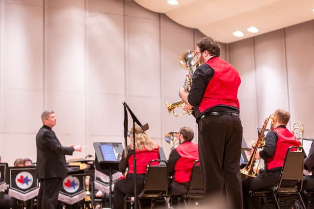 Standing euphonium soloist and conductor with a brass band in red vests on stage