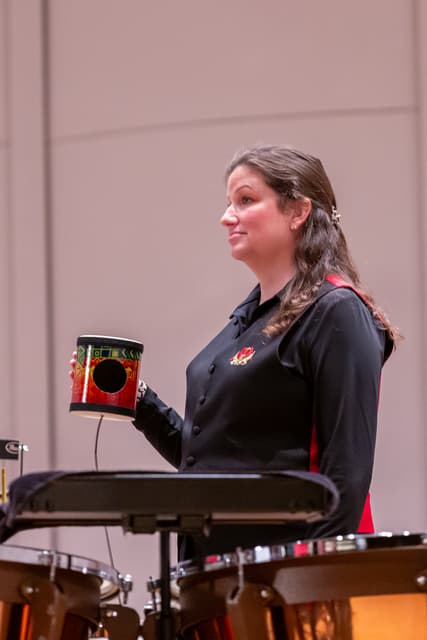 Percussionist on stage holding a colorful drum behind timpani