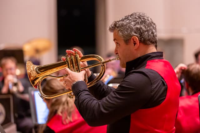 Flugelhorn player in red vest performing with a brass band on stage