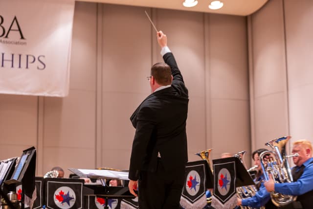 Conductor seen from behind raising a baton in front of a brass band on stage