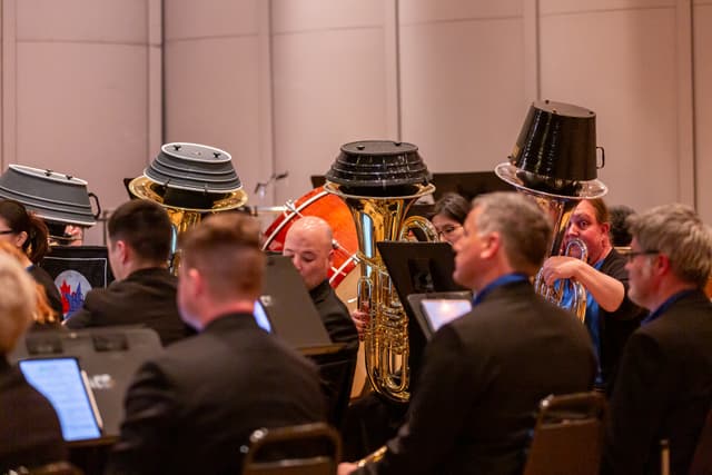 Tubas fitted with large black mutes beside a bass drum and seated band musicians