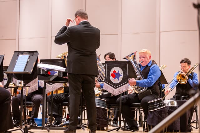 Conductor from behind leads brass band with euphonium and trombone players on stage
